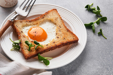 Breakfast on Valentines Day. Heart shaped egg with toast and microgreens on light grey background, breakfast table top. Valentines day breakfast. Top view. Mock up.