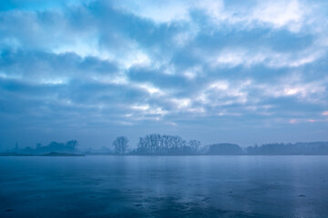 Hazy winter landscape of a frozen lake with trees on the shore