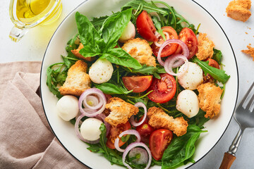 Panzanella Bread Salad. Traditional food of Italy with tomatoes, mozzarella balls, basil, onion and bread on light grey background. Traditional Italian cooking. Top view. Copy space.