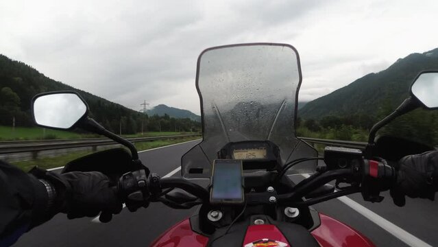 POV Biker rides a motorcycle on a highway in heavy rain with fog by Austria mountains. Scenic mountain road in Storm. Steering wheel view. First-person view. Solo motorcycle travel in bad weather.