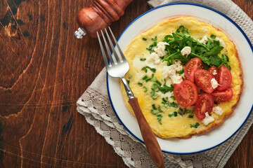 Rustic omelette or frittatas with green onions, cheese mozzarella, green arugula and tomatoes on old wooden dark background. Healthy food concept. Breakfast. Copy space. Top view. Mock up.