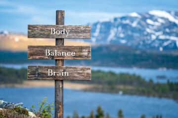 body balance brain text quote engraved on wooden signpost outdoors in the wilderness. Mountains and lakes in the background.