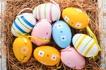 Easter holiday. Colorful Easter eggs in wooden basket on white wooden background. Easter greeting card. Top view, copy space.