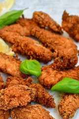 
 Crispy  deep fried   chicken strips and wings . Breaded  with cornflakes chicken  breast fillets  with lemons s and fresh   basil on wooden rustic background