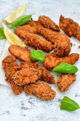 
 Crispy  deep fried   chicken strips and wings . Breaded  with cornflakes chicken  breast fillets  with lemons s and fresh   basil on wooden rustic background
