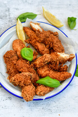 
 Crispy  deep fried   chicken strips and wedges potato. Breaded  with cornflakes chicken  breast fillets  with chilly peppers and fresh   basil on wooden rustic background