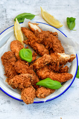 
 Crispy  deep fried   chicken strips and wedges potato. Breaded  with cornflakes chicken  breast fillets  with chilly peppers and fresh   basil on wooden rustic background