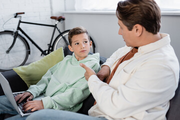 Obraz premium Kid using laptop near dad pointing with hand on couch