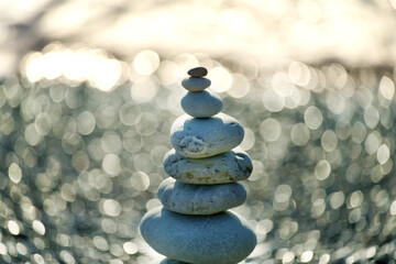 Pyramid of sea pebbles and sparkling sunny bokeh. Artistic photo. 