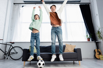 Cheerful father and son watching football match and jumping at home