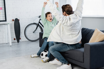 Boy and dad showing yes gesture near football ball at home