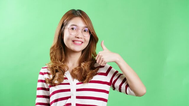 Cheerful young Asian woman with eyeglasses raising hands up, shaking and having fist pump from happiness, smiling woman face, green screen background.