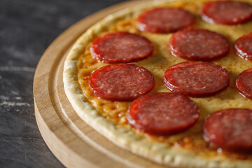 Pepperoni pizza, uncut on wooden stand on dark background, selective focus.