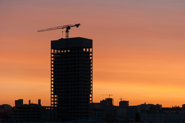 Fototapeta na wymiar Construction crane together with a new skyscraper during construction against the backdrop of sunset.