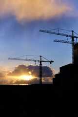 Silhouette industrial crane construction site with sunset and clouds in the background