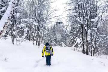 backpacker walks along a path in a winter forest, following a quadcopter