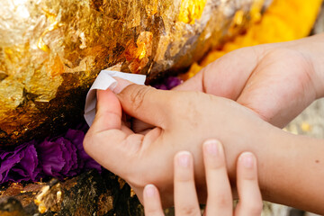 Hands mother and daughter affixing gold leaf to  Buddha statue. Kid girl hand touching onto hand...