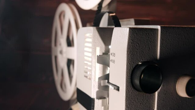  Old-fashioned 8mm film projector demonstrating tape movie. Projecting beam of light. Home theater, broadcasting, coils rotating. Entertainment, nostalgia, festival equipment concept