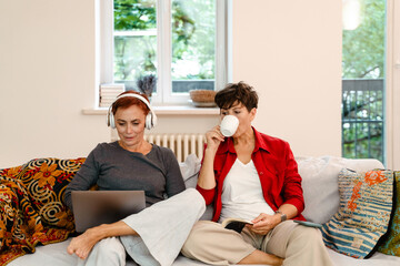 Mature lesbian couple using laptop and drinking coffee on sofa