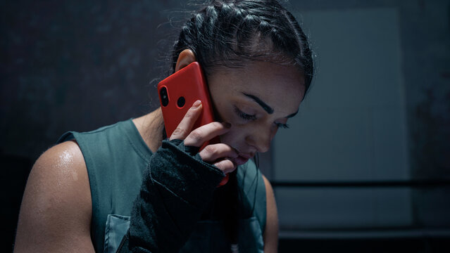 Young Isolated Ethnic Female Kick Boxer With Braids Using a Smartphone, Calling Her Family in Between Training and Sparring Sessions Preparing for a Boxing Match. Confident Woman Boxer Isolated.