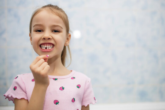 Girl child shows mouth without one lost baby tooth. A child in the bathroom holds a milk tooth in his hand. Free space for text or advertisement for designer
