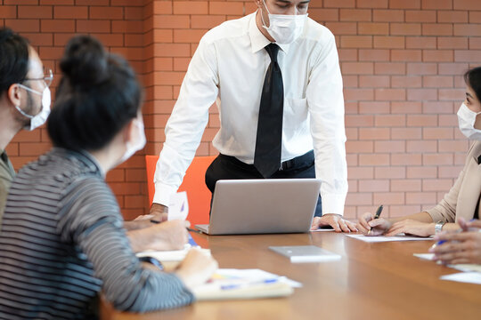 Supervisor or team leader giving some new ideas and advice about project to his partners in conference room and business people discussing new project in office wear mask to protect covid-19