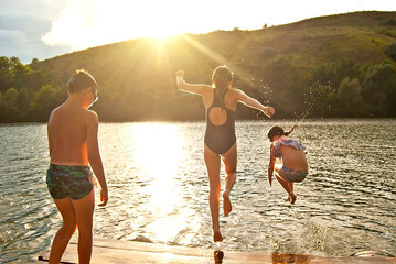 Children jump into the water from the pier. Camping by the water. Active rest on a sunset background. Concept of summer, vacation, travel and vacation.