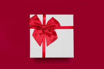 White gift box with a ribbon and a bow on a red background. A gift for a birthday or a traditional holiday. Gift box close up