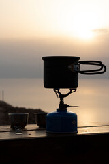 Naklejka premium Making coffee outdoors on gas camping fire during beautiful sunrise