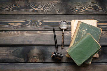 Stack of old books, quill pen and magnifying glass on the writer table flat lay background with...
