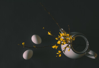 a branch with yellow forsythia flowers in a teapot, eggs