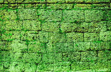 Stone masonry of walls and fences of ancient fortress structures covered with green moss. The ancient city of Angkor wat in Cambodia. Background wall with texture of green moss and plants.