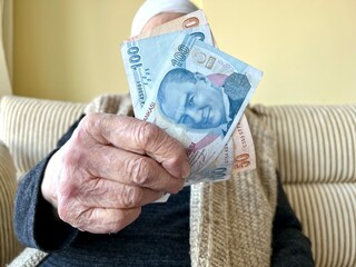 wrinkled hands of old person holding some turkish lira banknotes