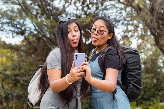 Retrato de dos hermosas chicas tomándose fotos en un parque,
Amigas felices revisando teléfono inteligente en aire libre,Dos chicas usando el móvil en medio de un camino rodeado de montañas
