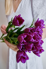 Happy woman holds purple tulips in her hands. Florist girl gathered a bouquet. Beautiful lavender flowers. Blossom petal. Gift for the holiday celebration, springtime mood. Romantic surprise

