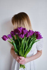 Happy woman holds purple tulips in her hands. Florist girl gathered a bouquet. Beautiful lavender flowers. Blossom petal. Gift for the holiday celebration, springtime mood. Romantic surprise

