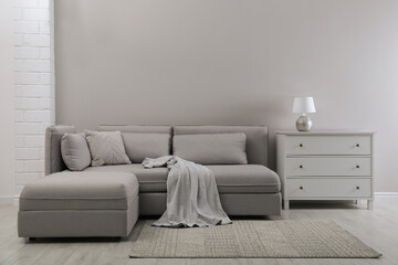 Large grey sofa and chest of drawers near light wall in room. Interior design