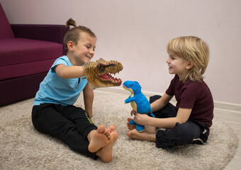 preschool boys play role-playing games with dinosaur toys sitting on the floor in the...