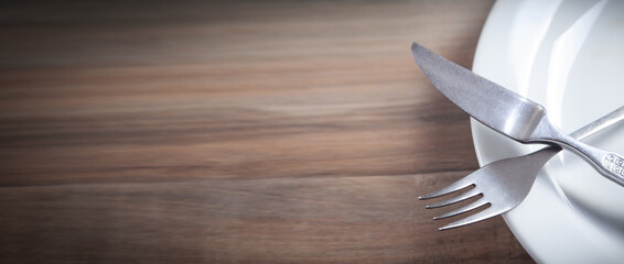 Empty plate with fork and knife on wooden table.