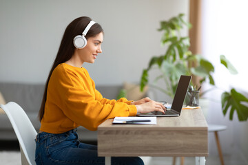 Young Caucasian lady in headphones using laptop pc, working online from home, copy space
