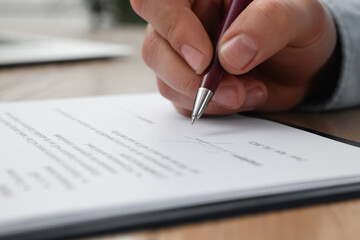 Man signing contract at table in office, closeup