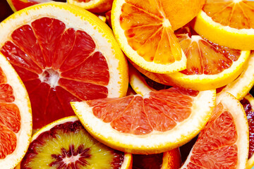 Whole and sliced juicy red oranges and grapefruits on a blue background.