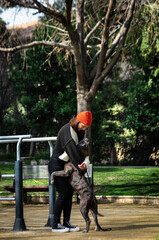 Una linda y alegre mujer caucásica en el parque jugando con su perro marrón de la raza American Stafford Terrier
