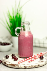 A bottle of cherry smoothies on a white background, cherries in bulk and in a plate. Morning summer breakfast