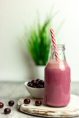 A bottle of cherry smoothies on a white background, cherries in bulk and in a plate. Morning summer breakfast