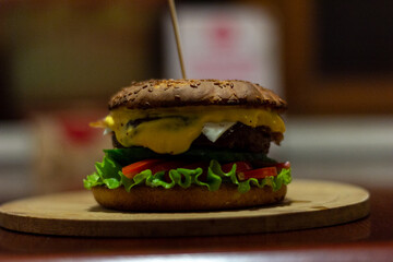 Burger from a meat patty with fresh cucumbers, tomatoes and cheese. White bun sprinkled with sesame seeds. Close-up