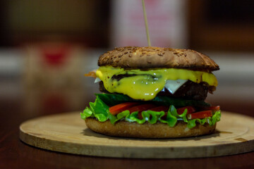 Burger from a meat patty with fresh cucumbers, tomatoes and cheese. White bun sprinkled with sesame seeds. Close-up