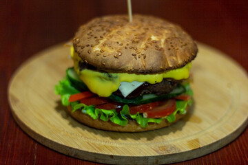 Burger from a meat patty with fresh cucumbers, tomatoes and cheese. White bun sprinkled with sesame seeds. Close-up