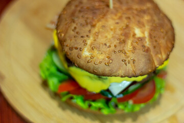 Burger from a meat patty with fresh cucumbers, tomatoes and cheese. White bun sprinkled with sesame seeds. Close-up
