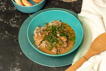 Buckwheat with meat and sauce in a blue plate, sprinkled with herbs. On a dark table. The concept of lunch, or a hearty dinner